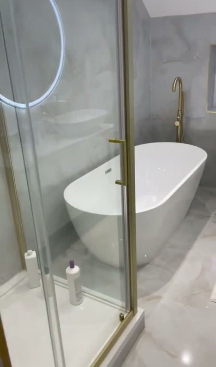 A bathroom with a freestanding bath, a glass shower with a gold frame and gold taps