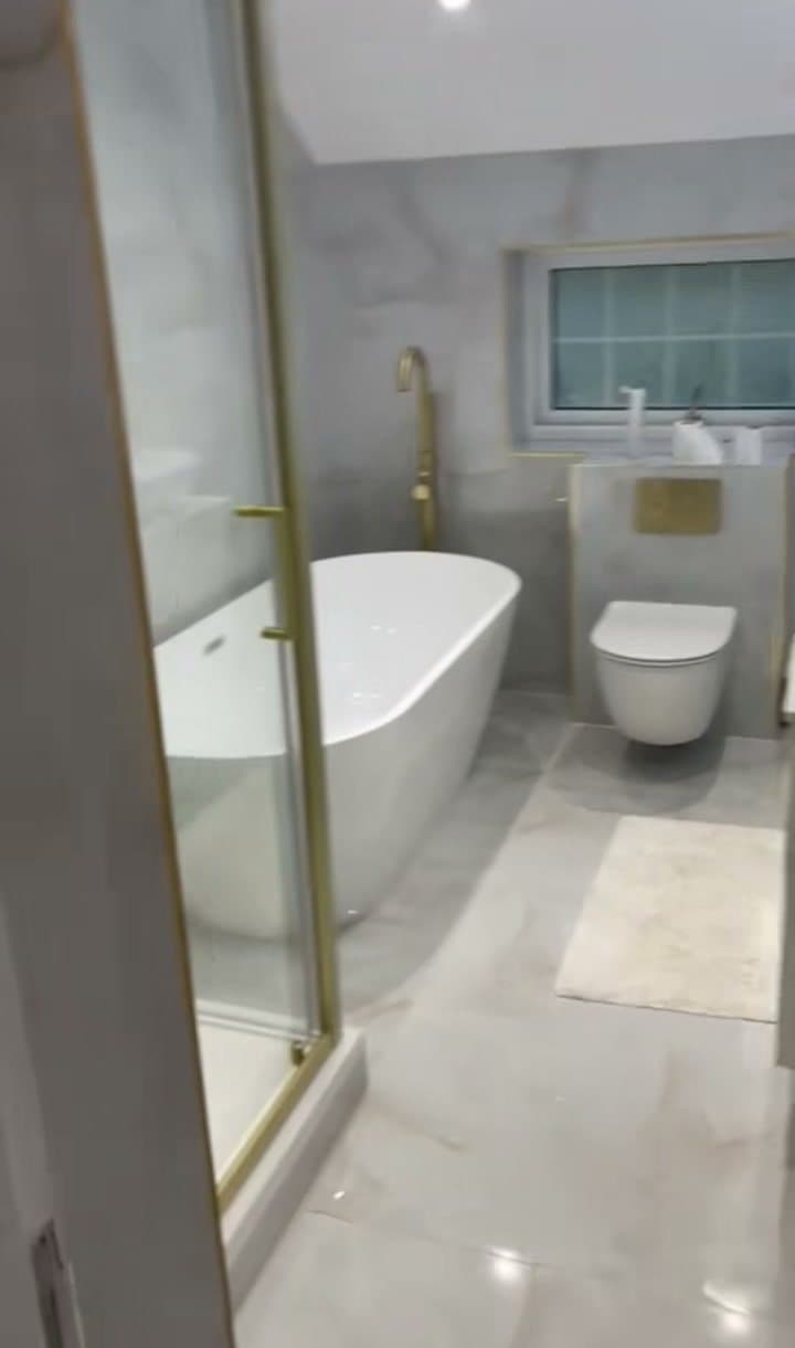 A walk-in shower with a gold frame next to a freestanding bath