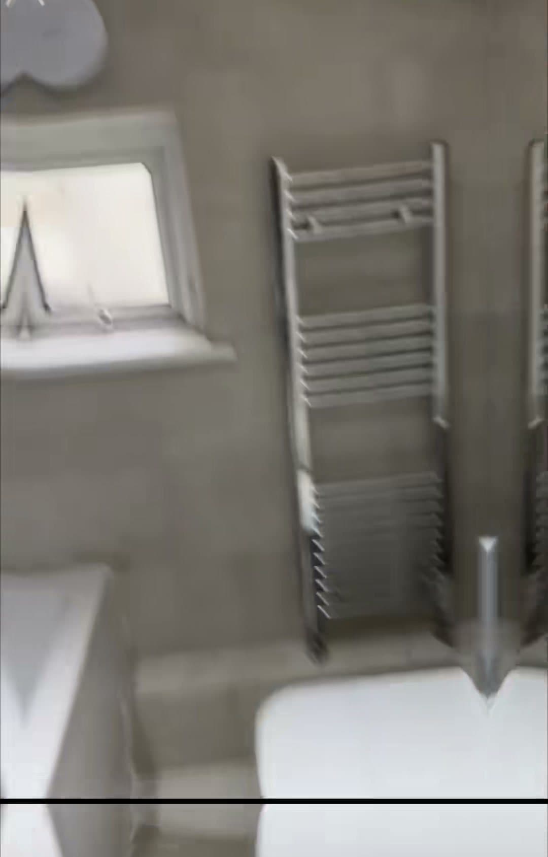 A bathroom with large grey tiles and a chrome towel rail