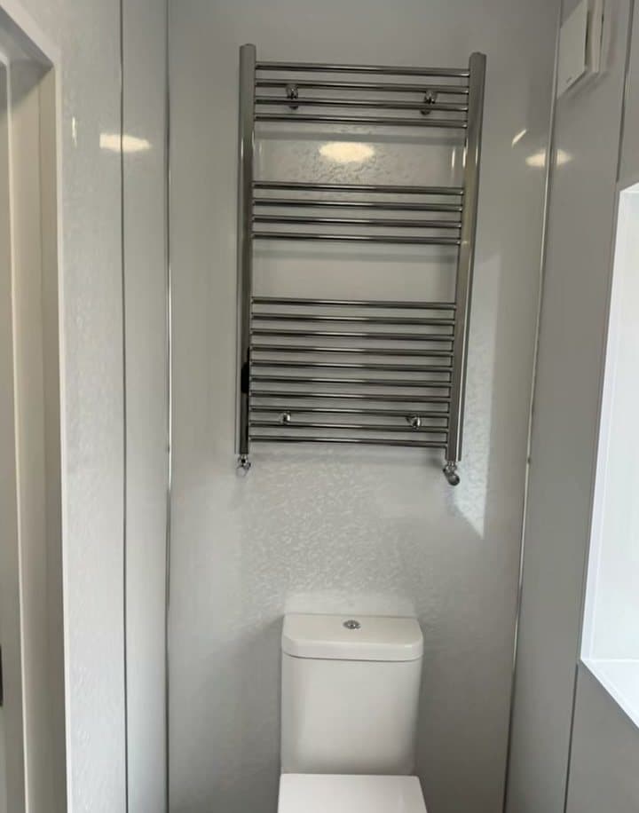 A compact white shower room with a towel rail and toilet