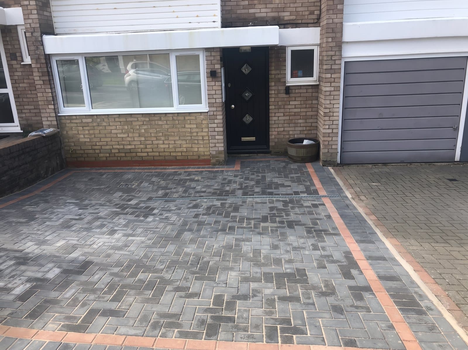 A grey block-paved driveway with a red border in front of a brick house