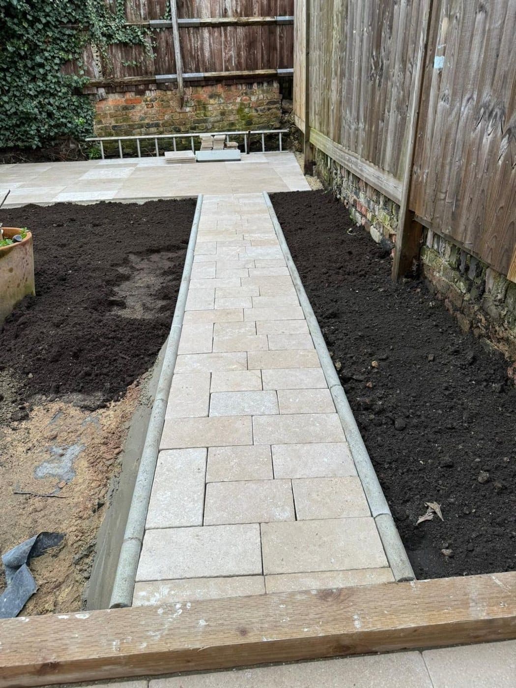 A pale stone path between two timber raised beds