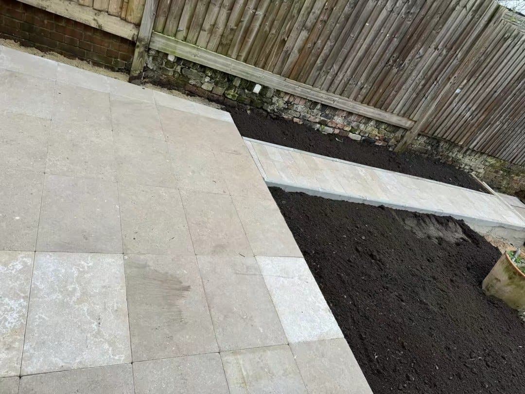 A finished stone patio with new planting beds along a garden fence